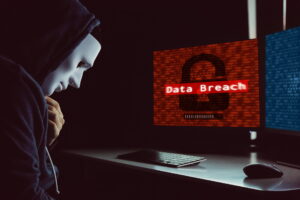 Masked hacker under hood using computer to commit data breach crime - internet computer crime concept